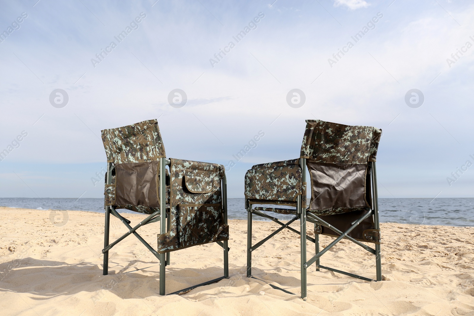 Photo of Comfortable camouflage fishing chairs on sandy beach near sea