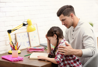 Photo of Man helping his daughter with homework at table indoors