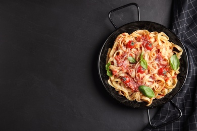 Photo of Tasty pasta and napkin on black table, flat lay. Space for text