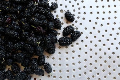 Photo of Heap of delicious ripe black mulberries in colander, top view. Space for text