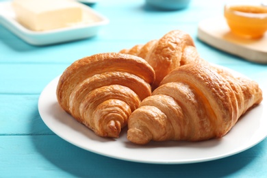 Photo of Plate with tasty croissants on light blue wooden table, closeup. French pastry