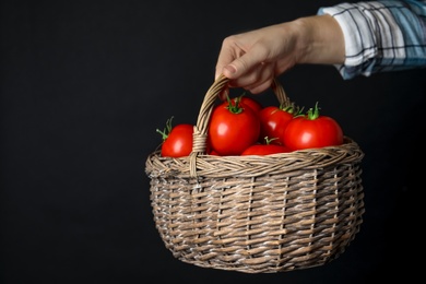 Woman with basket of ripe tomatoes on black background, closeup