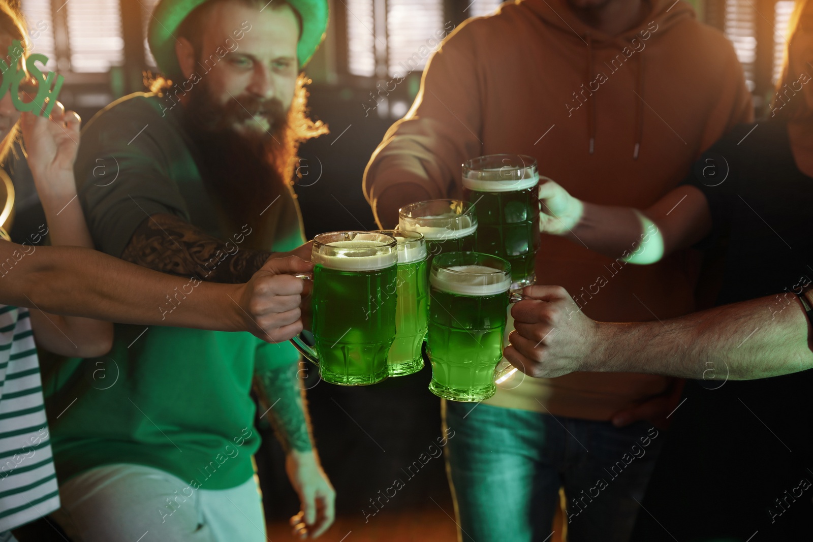 Photo of Group of friends toasting with green beer in pub, closeup. St. Patrick's Day celebration