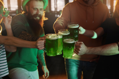 Group of friends toasting with green beer in pub, closeup. St. Patrick's Day celebration