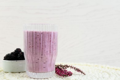 Photo of Glass of delicious blackberry smoothie, fresh berries and flowers on white wooden background. Space for text