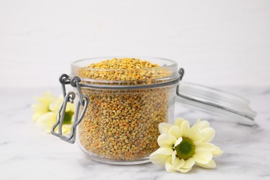 Fresh bee pollen granules in jar and flowers on light table, closeup