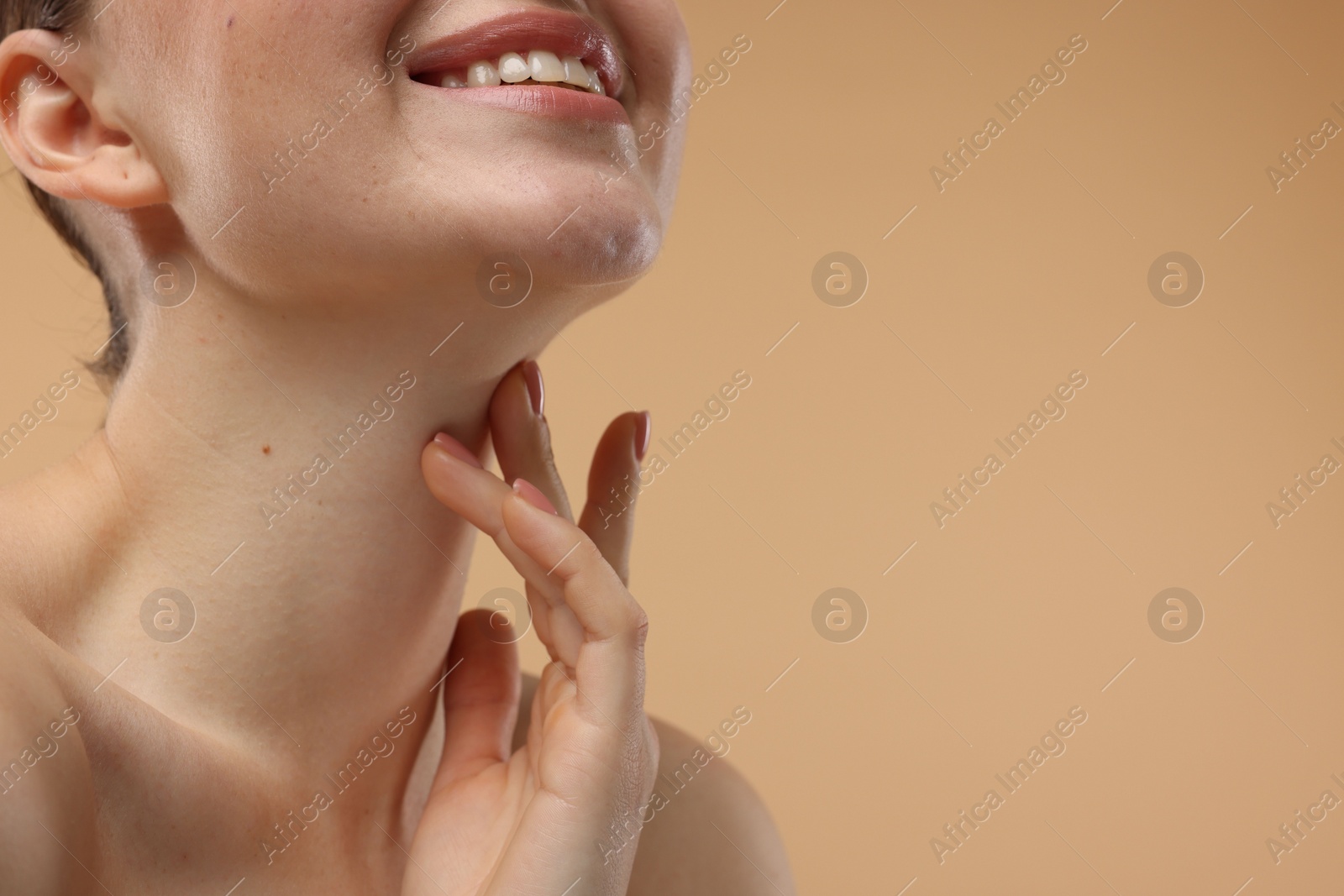 Photo of Smiling woman touching her neck on beige background, closeup. Space for text