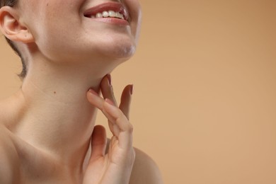 Photo of Smiling woman touching her neck on beige background, closeup. Space for text