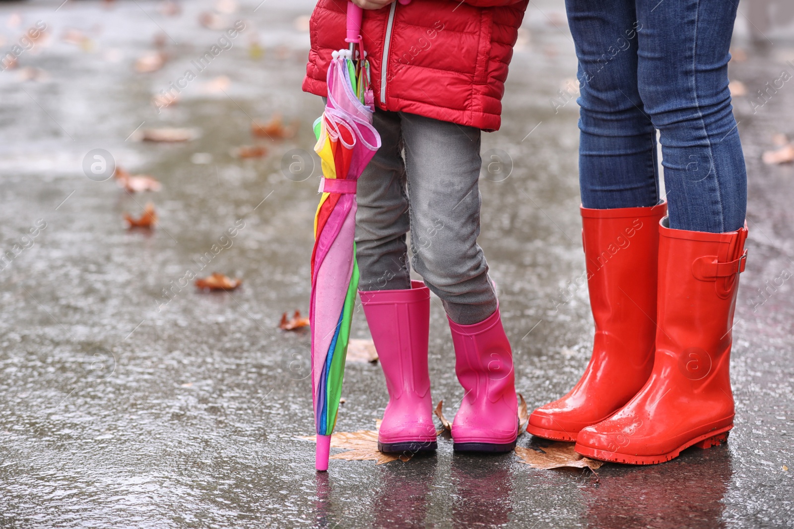 Photo of Mother and daughter with rubber boots and umbrella after rain, focus of legs. Autumn walk