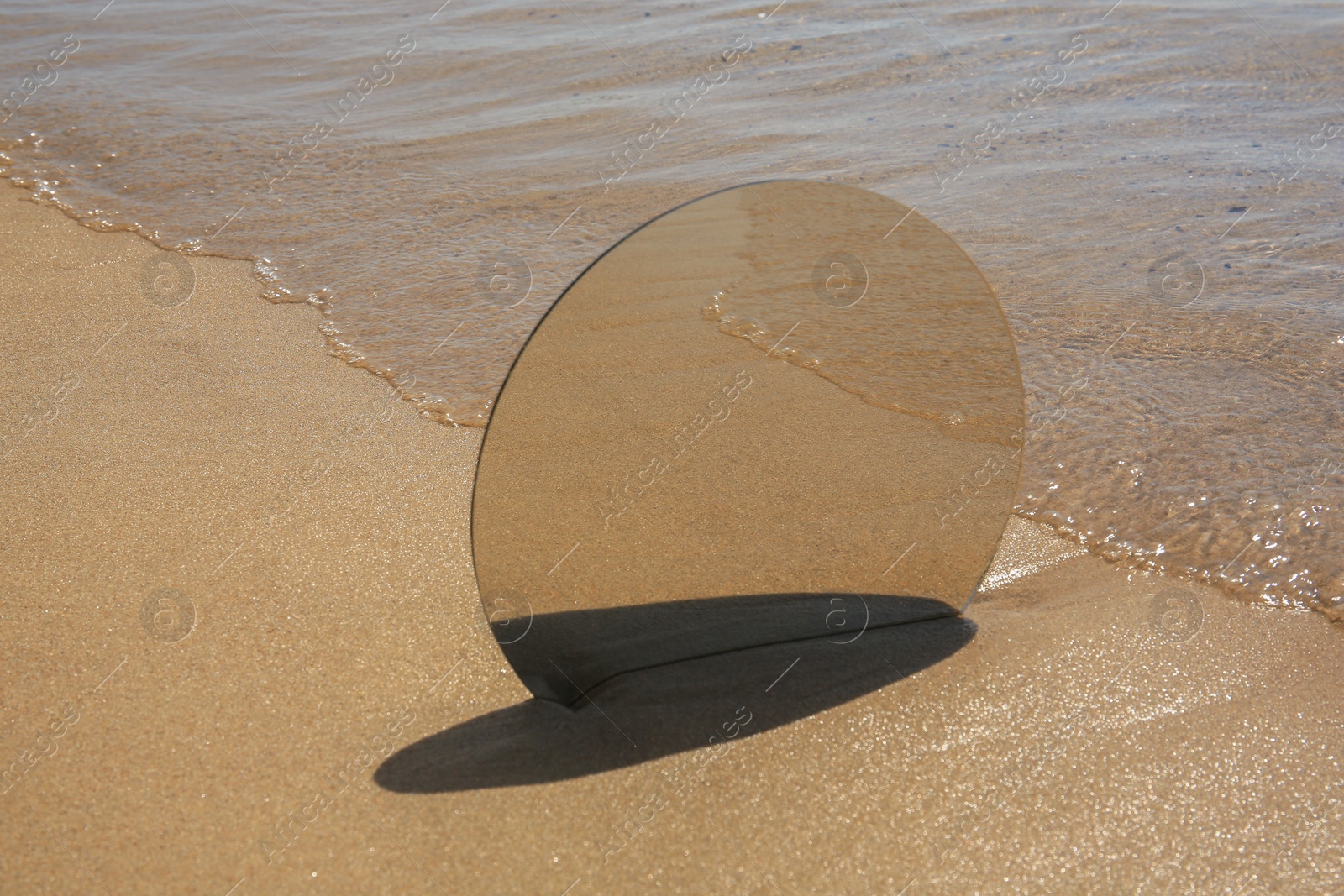 Photo of Round mirror reflecting sea on sandy beach