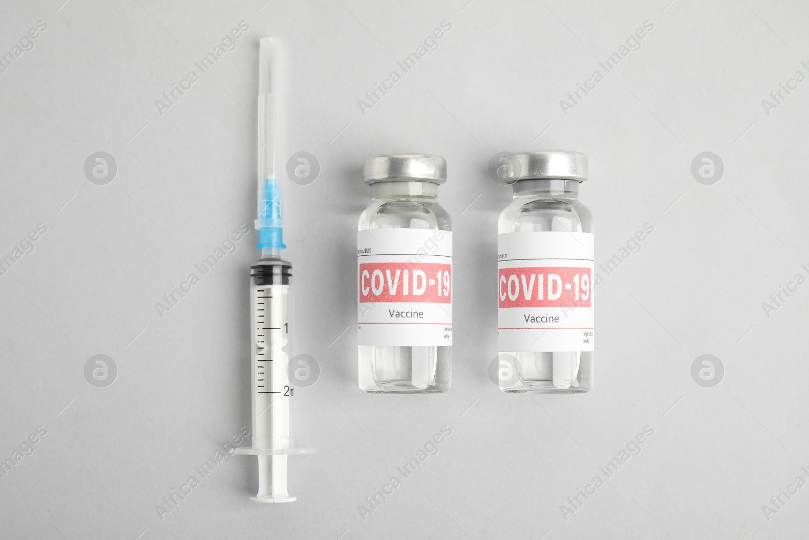 Photo of Vials with coronavirus vaccine and syringe on light background, flat lay