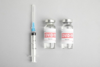 Photo of Vials with coronavirus vaccine and syringe on light background, flat lay