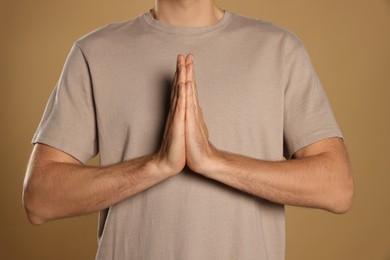 Photo of Man with clasped hands praying on beige background, closeup
