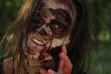 Scary zombie with bloody face outdoors, closeup. Halloween monster
