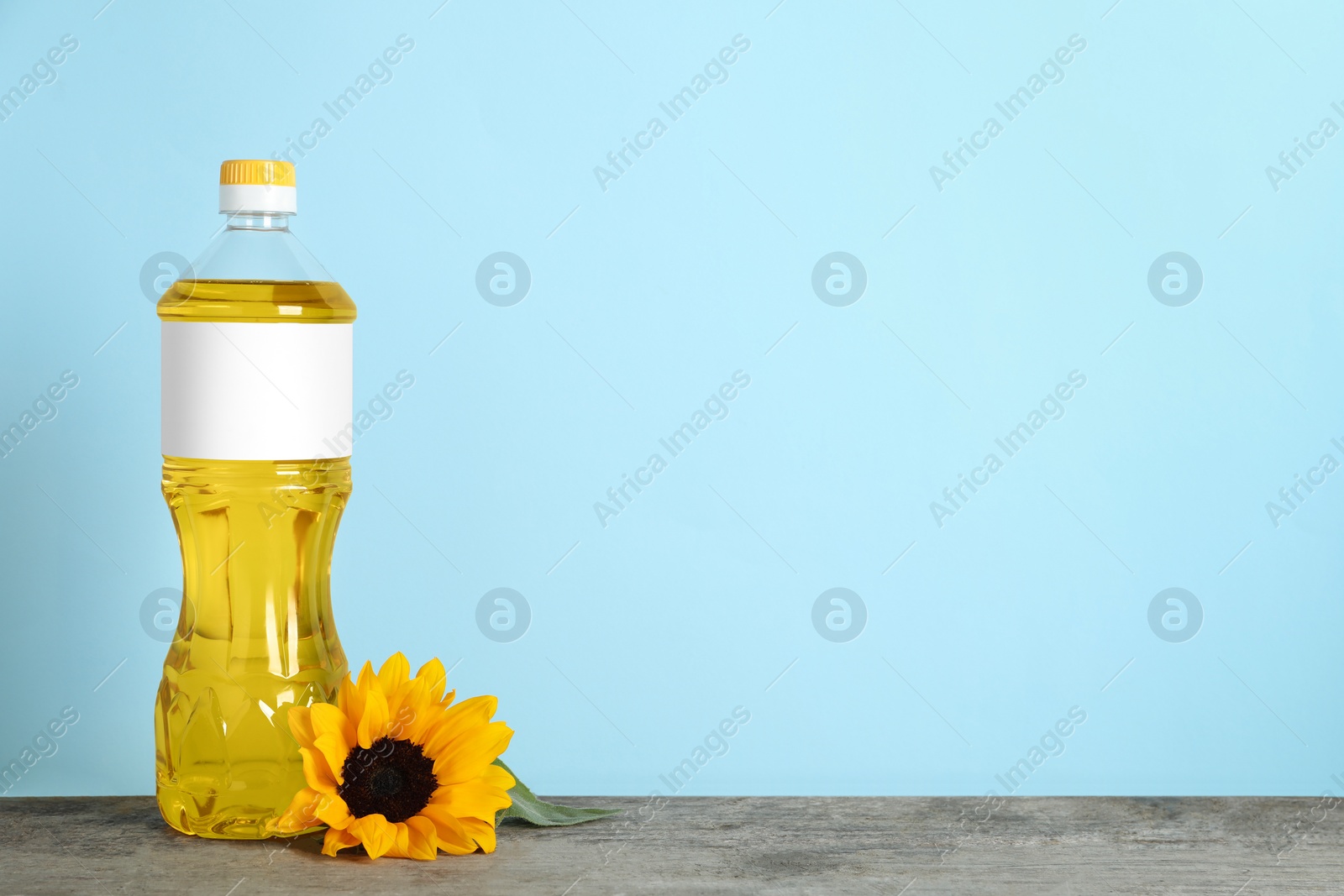 Photo of Bottle of cooking oil and sunflower on wooden table, space for text