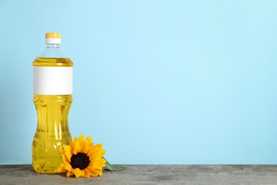 Photo of Bottle of cooking oil and sunflower on wooden table, space for text
