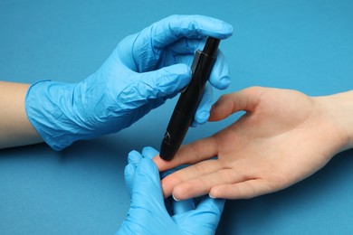 Photo of Diabetes. glucose testing. Doctor using lancet pen on blue background, closeup