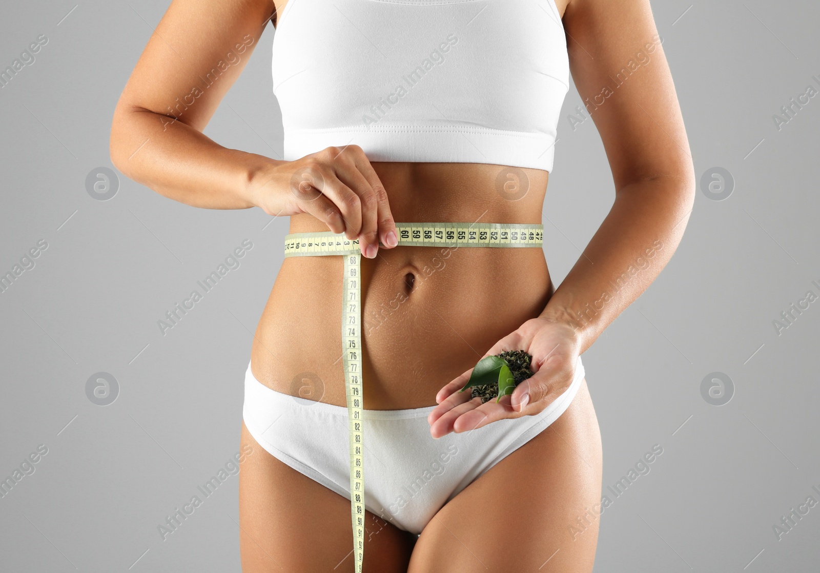 Photo of Young woman with measuring tape holding fresh and dry tea leaves on grey background, closeup