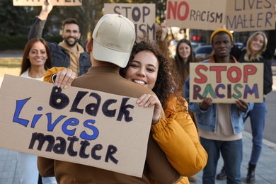 Photo of African American woman hugging man and holding sign with phrase Black Lives Matter outdoors during anti racism protest