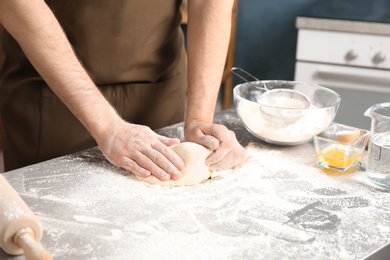 Photo of Man kneading dough on table covered with flour in kitchen