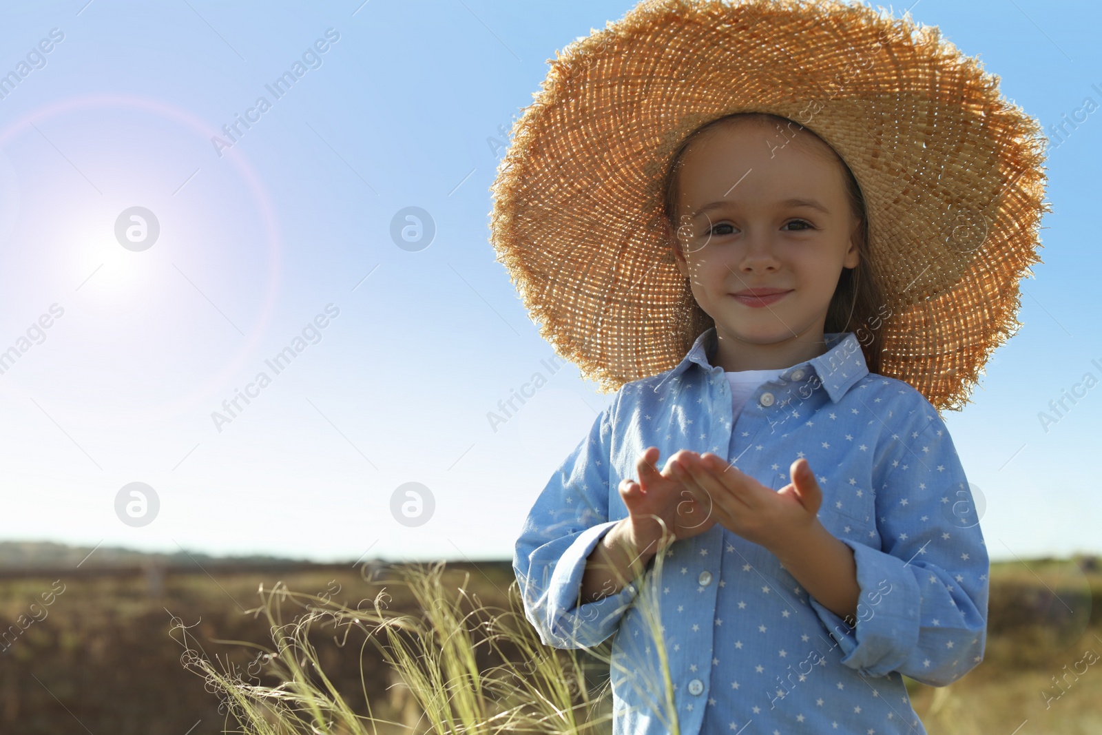 Photo of Cute little girl wearing straw hat outdoors, space for text. Child spending time in nature