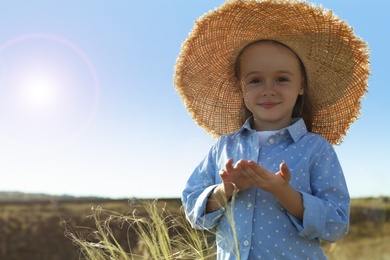 Photo of Cute little girl wearing straw hat outdoors, space for text. Child spending time in nature