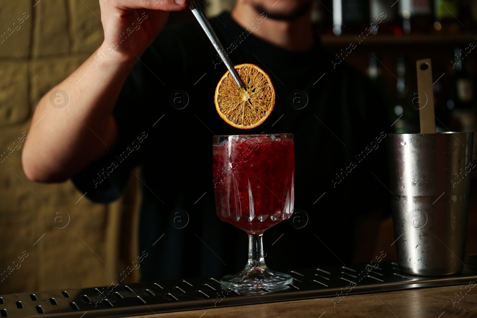 Photo of Bartender decorating glass of fresh alcoholic cocktail at bar counter, closeup