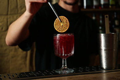 Bartender decorating glass of fresh alcoholic cocktail at bar counter, closeup