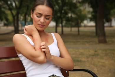 Photo of Woman scratching arm with insect bite in park. Space for text