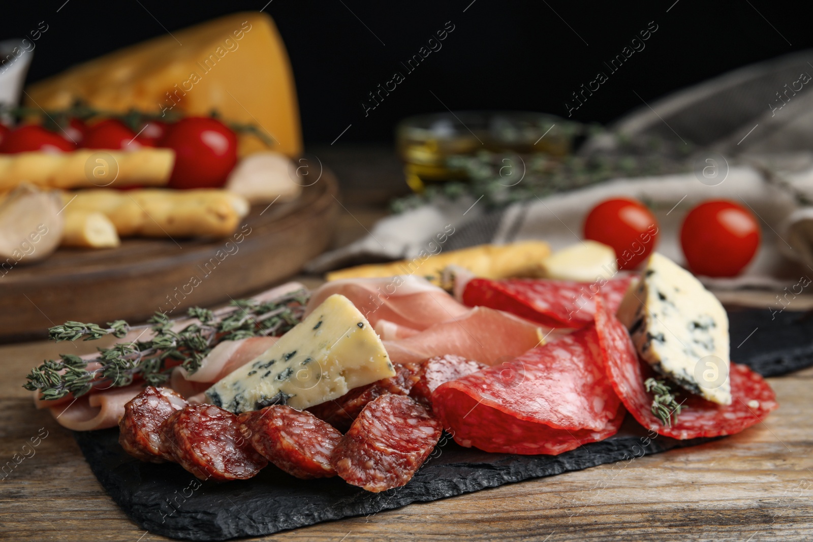 Photo of Tasty prosciutto with other delicacies served on wooden table, closeup