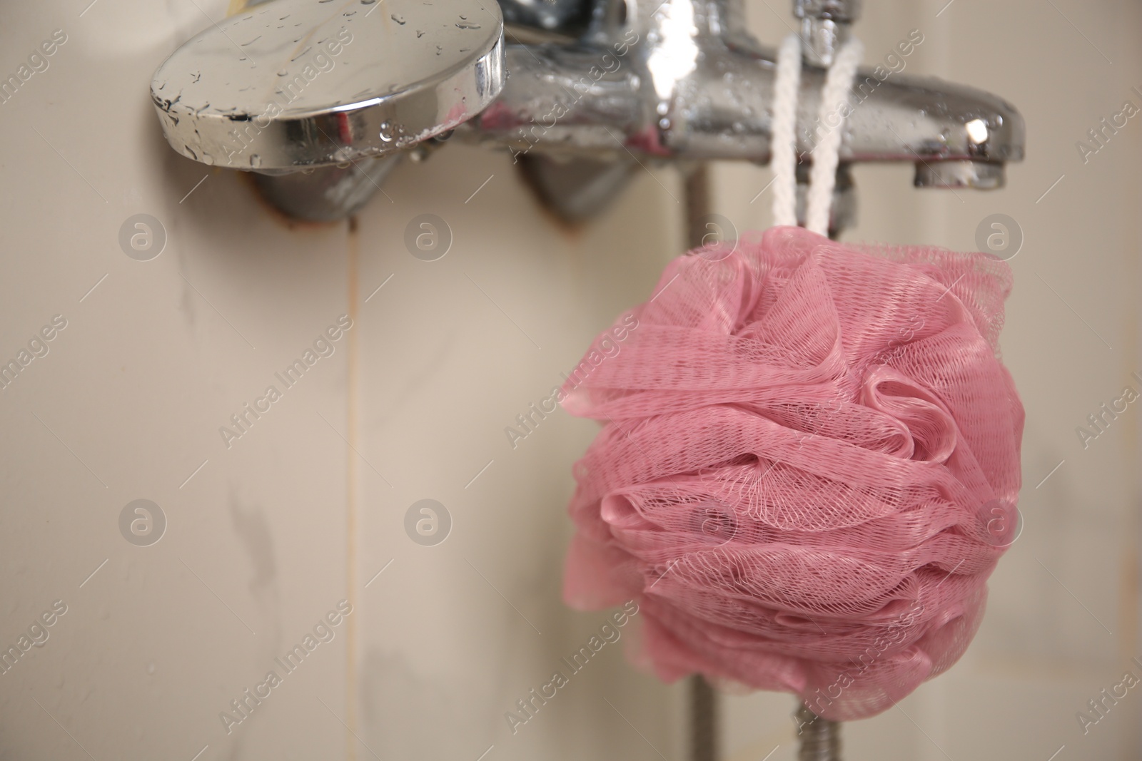 Photo of Pink shower puff hanging on faucet in bathroom, closeup