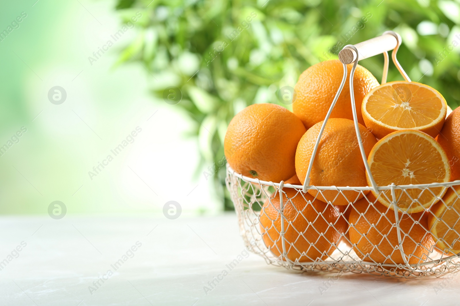 Photo of Basket with ripe oranges on table against blurred background. Space for text