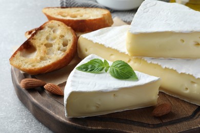 Tasty cut brie cheese with basil, bread and almonds on wooden board, closeup