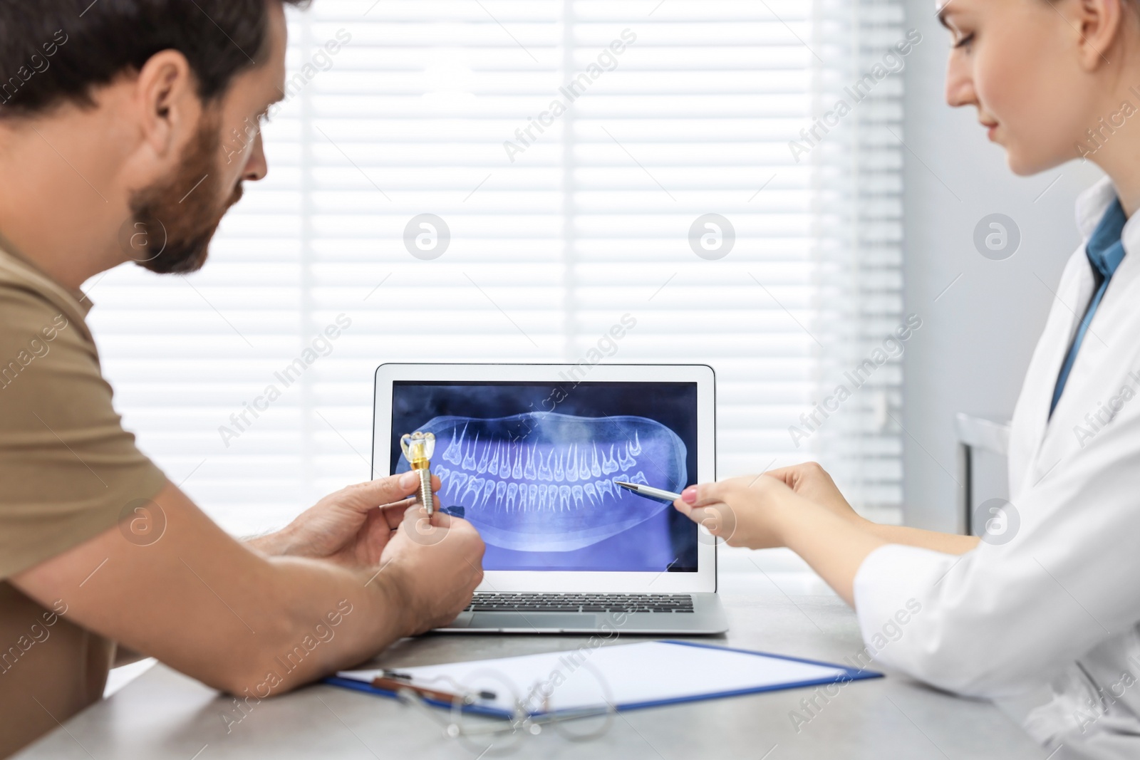 Photo of Doctor showing patient X-ray picture and educational model of dental implant in clinic, closeup