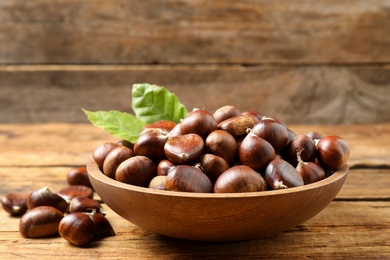Photo of Fresh sweet edible chestnuts in bowl on wooden table