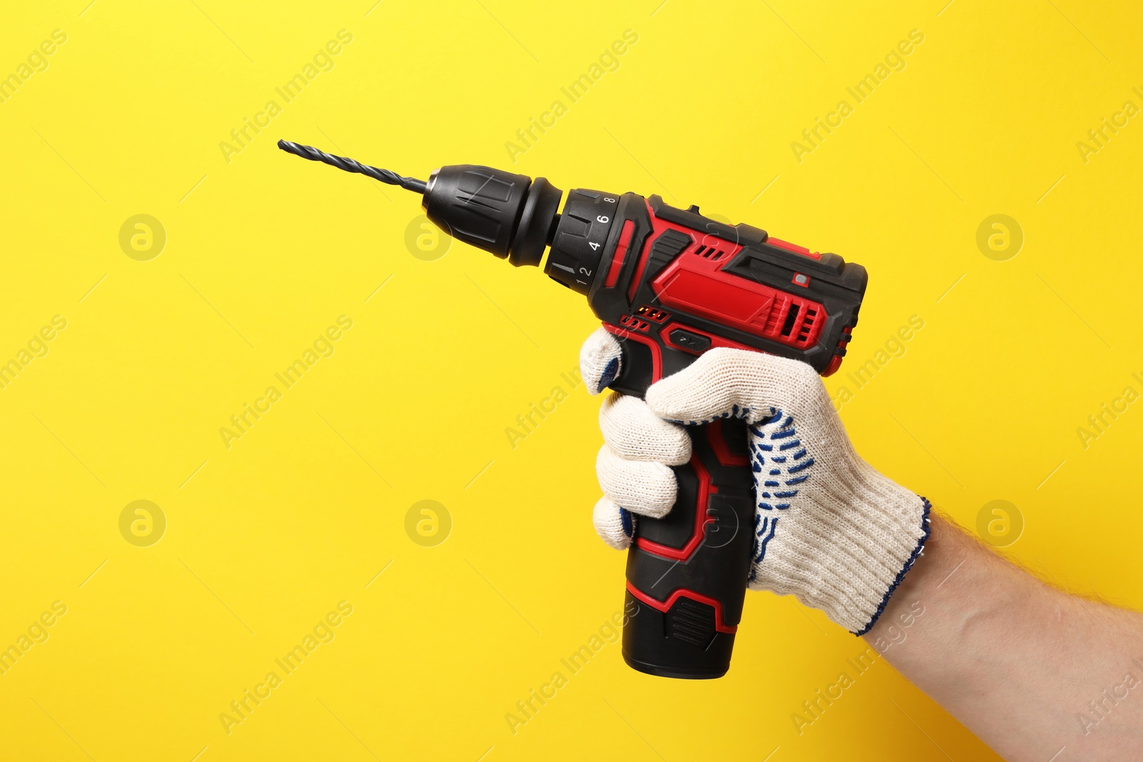 Photo of Handyman holding electric screwdriver on yellow background, closeup