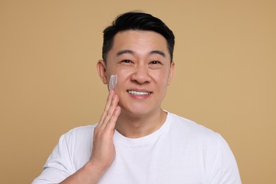 Photo of Handsome man applying cream onto his face on light brown background