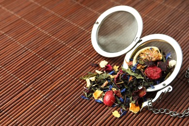 Photo of Snap infuser with dried herbal tea leaves and fruits on bamboo mat. Space for text