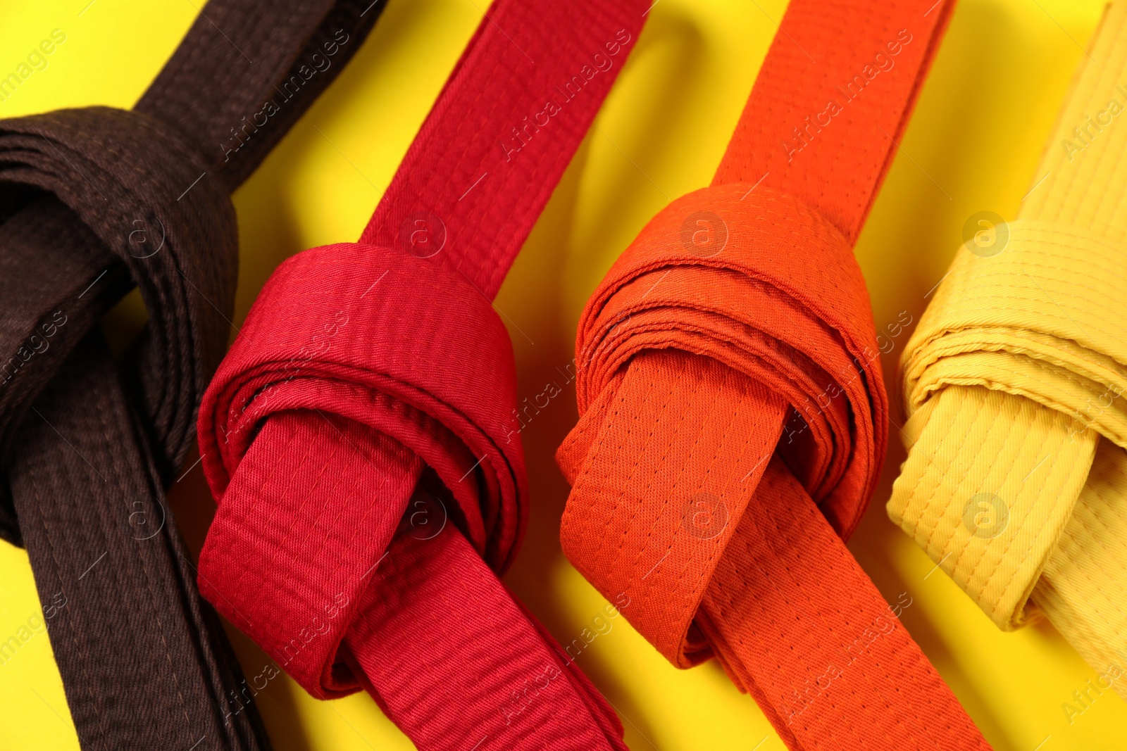 Photo of Colorful karate belts on yellow background, closeup