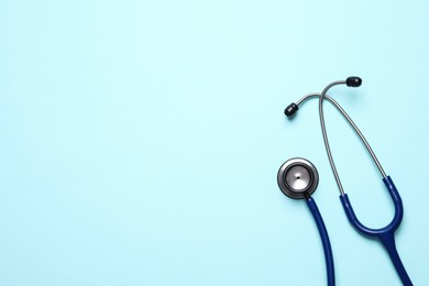 Stethoscope on light blue background, top view. Space for text