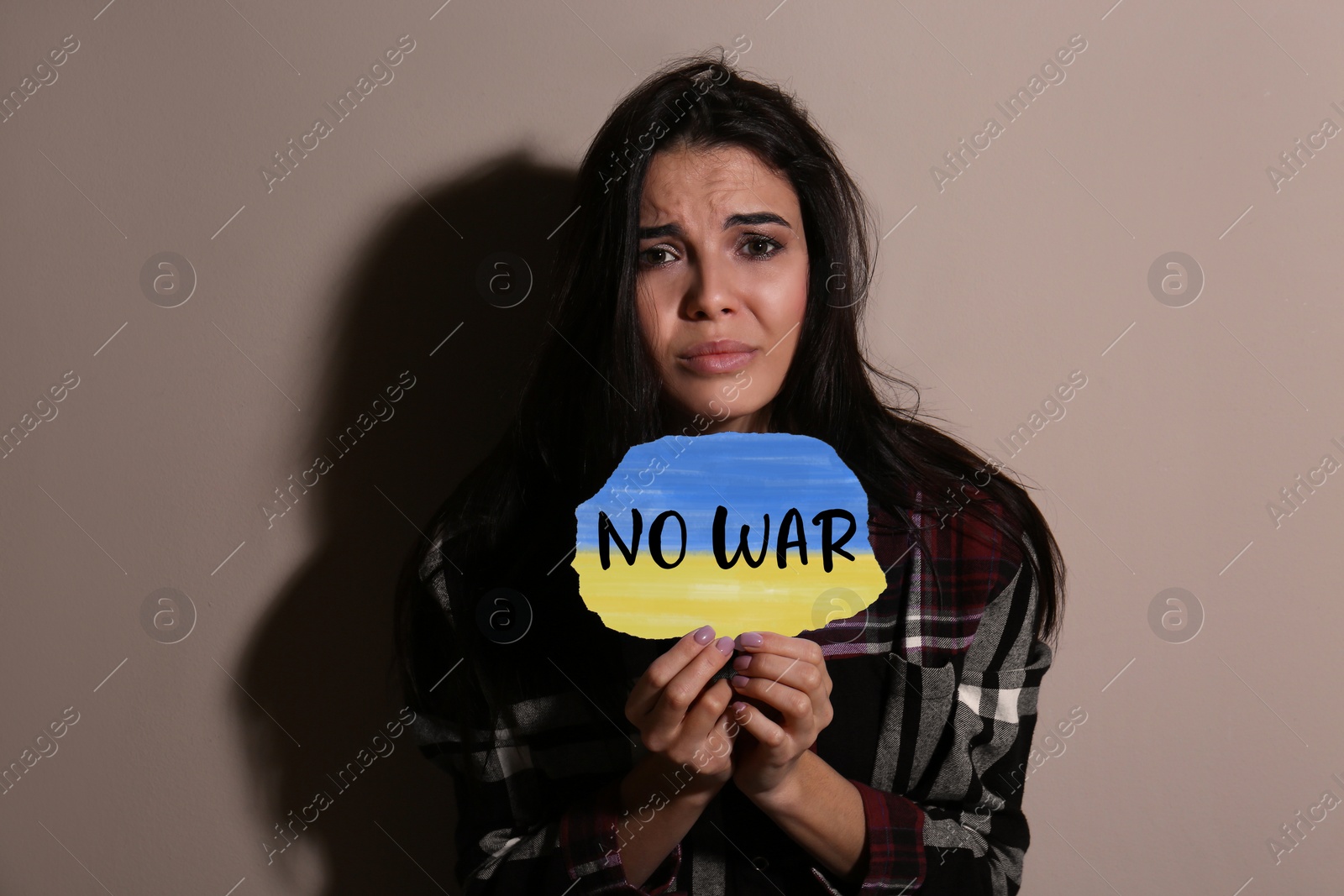 Image of Sad woman holding paper with phrase No War near beige wall