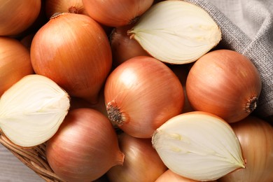 Wicker basket with whole and cut onions on table, top view