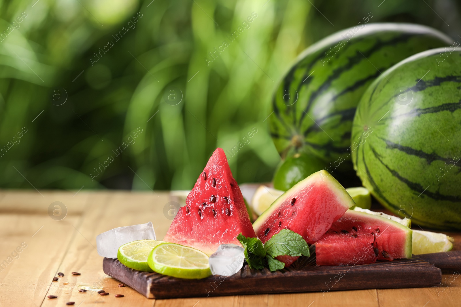 Photo of Slices of delicious ripe watermelon, ice cubes and cut lime on wooden table outdoors, space for text