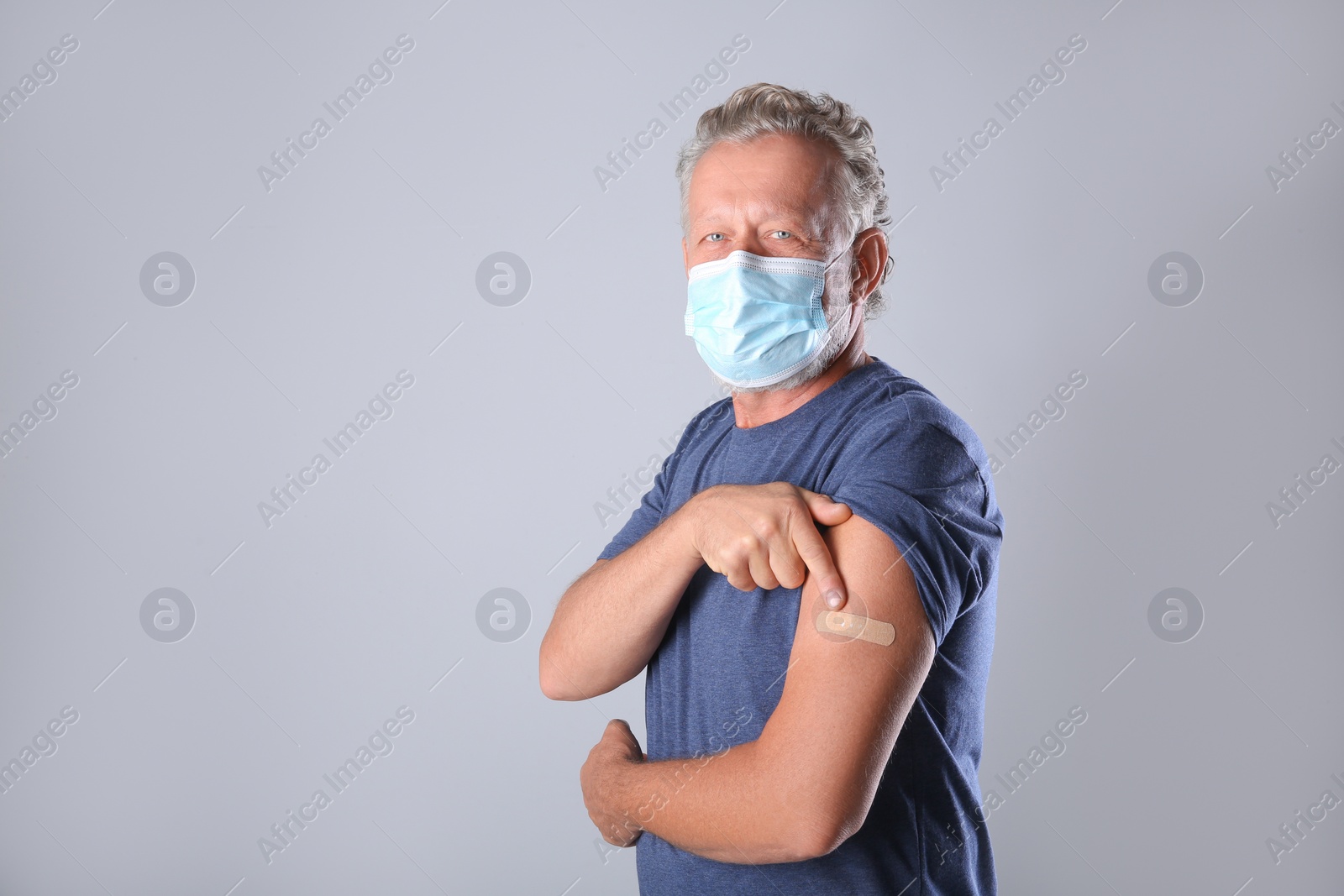 Photo of Senior man in protective mask pointing at arm with bandage after vaccination on grey background. Space for text