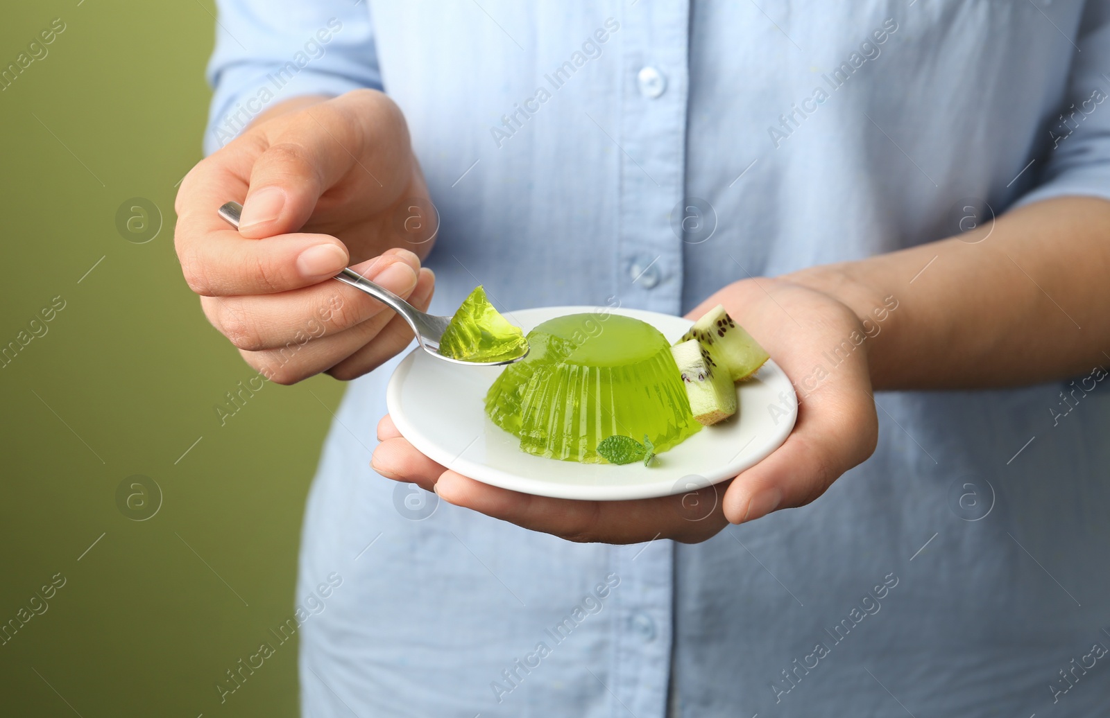 Photo of Young woman eating tasty kiwi jelly on green background, closeup