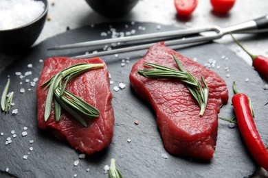 Photo of Fresh raw meat steaks and spices on slate plate, closeup