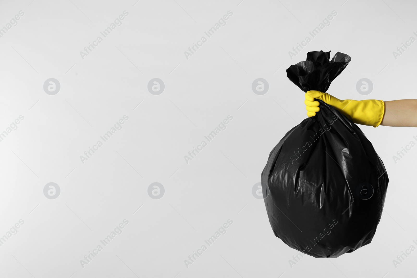 Photo of Janitor in rubber glove holding trash bag full of garbage on light grey background, closeup. Space for text