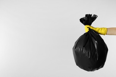 Photo of Janitor in rubber glove holding trash bag full of garbage on light grey background, closeup. Space for text