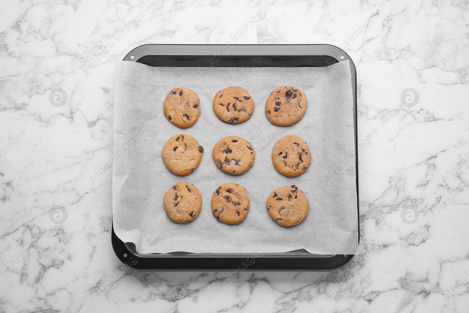 Photo of Baking pan with cookies and parchment paper on white marble table, top view