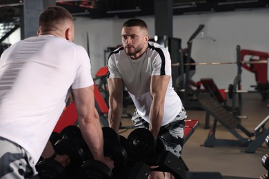 Photo of Man looking at mirror near dumbbells rack in gym